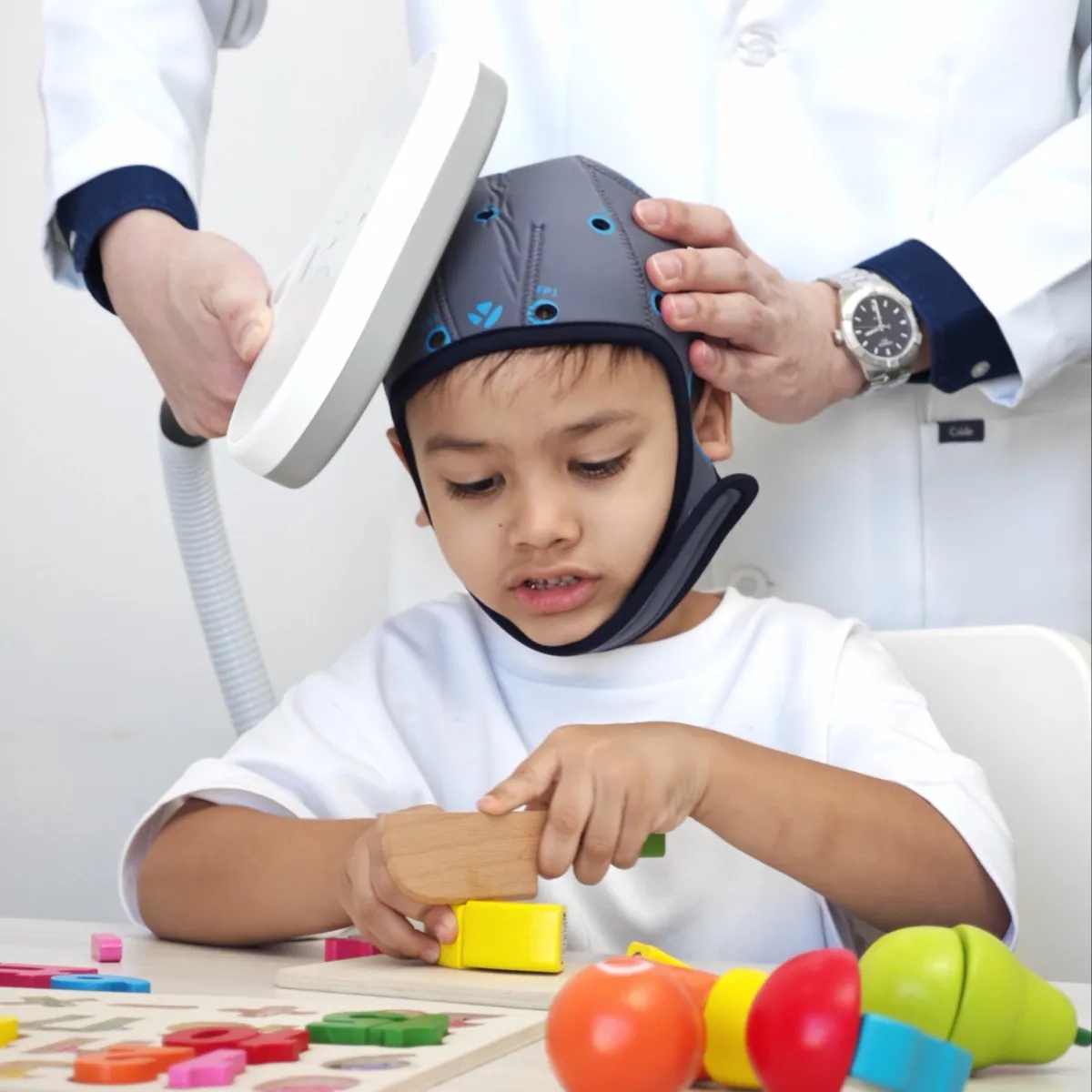 คุณหมอวางเครื่องกระตุ้นสมอง TMS ให้เด็ก ขณะเด็กเล่นของเล่นฝึกทักษะ ที่ InterRehab NeuroBridge
